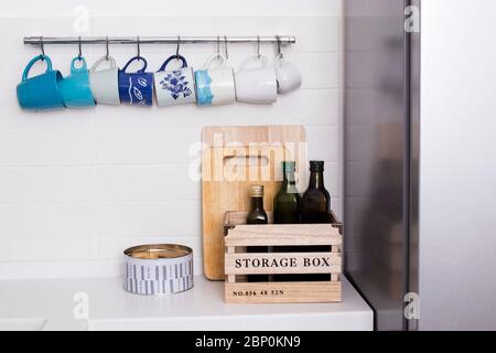 Mehrfarbige Keramiktassen in Blautönen hängen an Haken über dem Küchentisch. Flaschen mit Olivenöl stehen in einer Holzkiste. Stockfoto