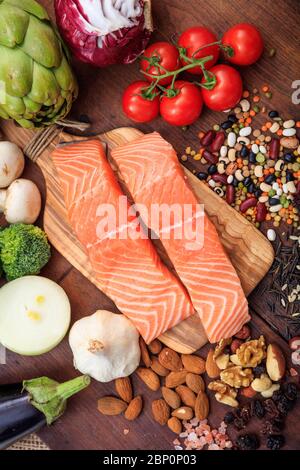 Lachsfischfilets auf Holzhintergrund. Zwei frische gesunde, ungekochte Fischscheiben auf Holzbrett, umgeben von Gemüse und Nüssen. Vertikal Stockfoto