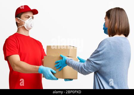 Selbstisolierung und Online-Shopping während der Quarantäne. Kurier in Schutzmaske und Handschuhen übergibt Pakete an Mädchen Client Stockfoto