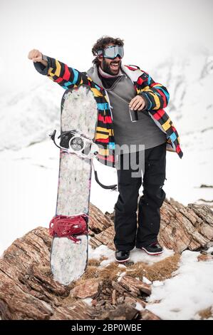 Fröhliche und positive Snowboarder posiert und genießt draußen, vor dem Hintergrund von schneebedeckten Gipfeln. Travel Lifestyle Konzept aktive Freizeit im Freien Stockfoto