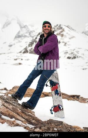 Fröhliche und positive Snowboarder posiert und genießt draußen, vor dem Hintergrund von schneebedeckten Gipfeln. Travel Lifestyle Konzept aktive Freizeit im Freien Stockfoto