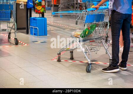 Mann, mit dem Einkaufswagen, Lebensmittel in einem Supermarkt während Coronavirus Covid-19 Pandemie. Klebeband am Boden zeigt die sichere soziale Distanz an Stockfoto