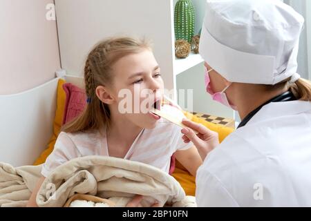 Kinderarzt untersucht die Kehle eines kleinen Mädchens zu Hause mit einem Zungendepressor Stockfoto