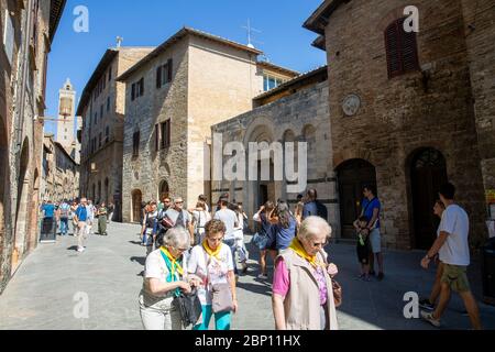 San Gimignano mittelalterliche Stadt auf einem Hügel in der Toskana, Touristen und Besucher spazieren durch die Stadtmauern und stöbern in der lokalen Architektur im sonnigen Italien Stockfoto