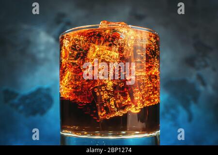 Glas mit Eiswürfeln und Blasen von frischen kohlensäurehaltigen Cola Soda trinken auf blauem Hintergrund, Makro-Foto Nahaufnahme. Stockfoto