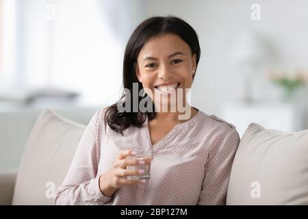 Frau auf dem Sofa sitzend, Glas Wasser haltend fühlt sich gesund an Stockfoto
