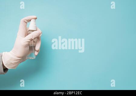 Hand der Frau in medizinischen Schutzhandschuh Hand hält Desinfektionsmittel Spay Flasche auf blauem Hintergrund Stockfoto