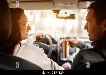 Glückliche junge Familie fährt in einem Auto im Wald. Eine Frau fährt ein Auto, und ein Mann sitzt in der Nähe. Anreise mit dem Auto Konzept. Stockfoto