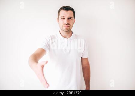 Junger Mann isoliert auf weißem Hintergrund. Guy halten Hand zum Schütteln gerade gerichtet. Fröhlicher positiver Mann allein im Studio Stockfoto