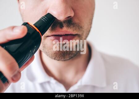 Junger Mann isoliert auf weißem Hintergrund. Nahaufnahme und Schnitt Blick auf Kerl entfernen Haare aus seiner Nase mit Trimmer. Genaue und sorgfältige Arbeit Stockfoto