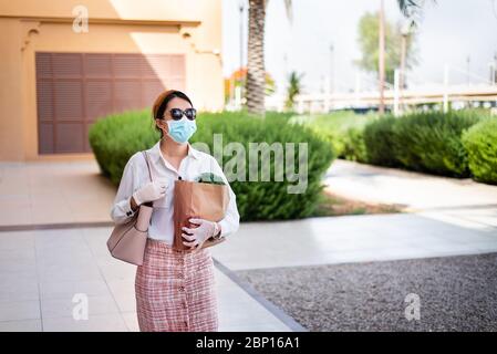 Asiatische Frau, die Einkaufstasche mit Lebensmitteln trägt, während sie Maske und Handschuhe trägt, um die Ausbreitung des Virus während der Coronavirus-Pandemie zu verhindern Stockfoto