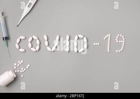 Flache Lage der Inschrift Covid-19 von Pillen, Spritze, Pillen und Thermometer auf grauem Hintergrund. Covid 19 aus, vor Viren und Bakterien schützen, bei h bleiben Stockfoto