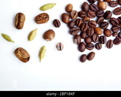 Flaches Lay. Kaffeebohnen und Kardamom-Körner sind auf einer weißen glänzenden Oberfläche verstreut. Geringe Schärfentiefe und stark verschwommener Hintergrund. Kopierbereich. Stockfoto