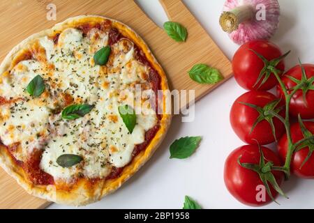 Hausgemachte italienische Pizza Napoletana mit frischen Tomaten und Knoblauch-Sauce, Mozarella-Käse und Basilikumblätter auf einem Holzbrett Draufsicht Stockfoto