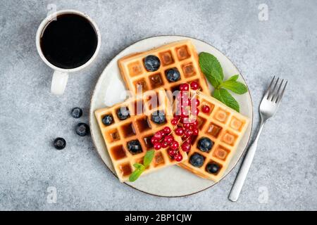 Waffeln mit Beeren und einer Tasse Kaffee. Süße belgische Waffeln mit Beeren, Sirup und schwarzem Couchtisch Draufsicht Stockfoto