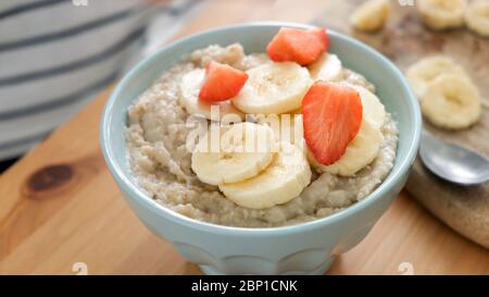 Haferbrei Haferbrei mit Banane, Erdbeeren in blauer Schale auf Holztisch. Gesundes Frühstück Stockfoto