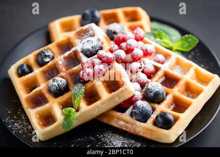 Quadratische belgische Waffeln mit Beeren und Zucker auf schwarzer Platte isoliert. Nahaufnahme. Süße Dessertwaffeln Stockfoto