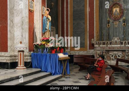 Eine ältere Frau, die mit einer Maske sitzt, betet vor der Statue der Jungfrau Maria während des Covid-19, wobei die Kirche nur für das persönliche Gebet geöffnet ist Stockfoto