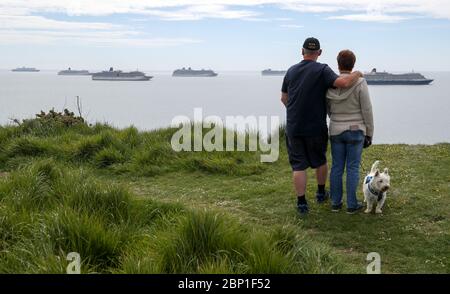 Die Leute schauen auf (von links nach rechts), die Cunard Cruise Liner Queen Mary 2 neben P&O Kreuzfahrtschiffen Aurora, Arcadia, Britannia und Azura und die Cunard Kreuzfahrtschiff Queen Victoria an Liegeplatz in Weymouth Bay. 6 Schiffe, darunter 5 Kreuzfahrtschiffe von P&O und Cunard und Cunard's Ocean Liner Queen Mary 2 haben in Weymouth Bay festgemacht, während die Kreuzfahrten wegen Coronavirus verschoben oder storniert werden. Stockfoto