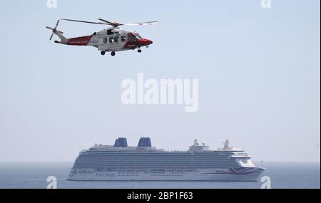 Ein Hubschrauber von her Majesty's Coast Guard fliegt über das P&O Kreuzfahrtschiff Azura (rechts) und das Cunard Kreuzfahrtschiff Queen Victoria am Liegeplatz in Weymouth Bay. 6 Schiffe, darunter 5 Kreuzfahrtschiffe von P&O und Cunard und Cunard's Ocean Liner Queen Mary 2 haben in Weymouth Bay festgemacht. 6 Schiffe, darunter 5 Kreuzfahrtschiffe von P&O und Cunard und Cunard's Ocean Liner Queen Mary 2 haben in Weymouth Bay festgemacht, während die Kreuzfahrten wegen Coronavirus verschoben oder storniert werden. Stockfoto