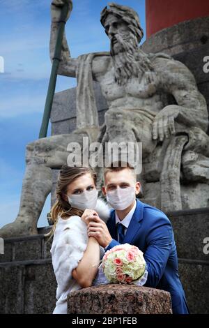 Frisch Vermählte gehen während der Isolation wegen der Coronavirus-Infektion Covid-19 Pandemie, sie tragen schützende chirurgische Masken, Hochzeitssaison Sommer Stockfoto