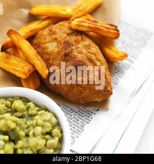 Zerschlagene Schellfisch Filet mit Bierteig Chips auf Zeitung mit Schüssel matschig Peas Stockfoto