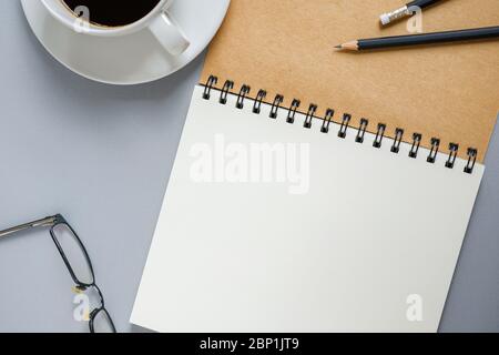 Draufsicht. Blank offenes Spiralheft, Bleistifte, Gläser und eine Tasse Kaffee in Arbeitszeitstimmung. Leer für Ihren Text. Stockfoto