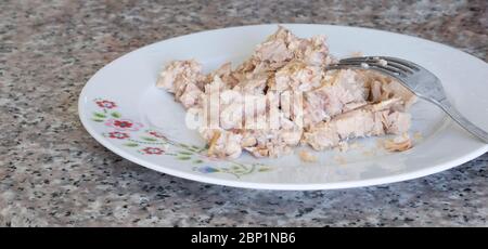 Thunfisch in der Dose ist in einem Porzellanteller und es gibt eine Gabel. Nahaufnahme. Stockfoto