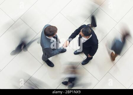 Geschäftsleute, die sich in einer Menge von Menschen, die sich zu Fuß befinden, die Hände schütteln, Draufsicht Stockfoto