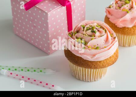 Rosa Cupcakes mit Geschenkbox und Geburtstagskerzen auf weißem Hintergrund - süße Muffins mit Pistazien-Streuseln verziert - selektiver Fokus Stockfoto