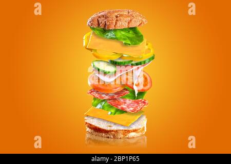 Leckeres Sandwich. Sandwich mit fliegenden Zutaten auf orangefarbenem Hintergrund isoliert. Stockfoto