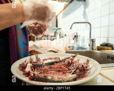 Hände des älteren Hauswirbes rentatfrau trägt transparente Handschuhe Reinigung Sardellen Fisch aus Kopf und Eingeweide Stockfoto