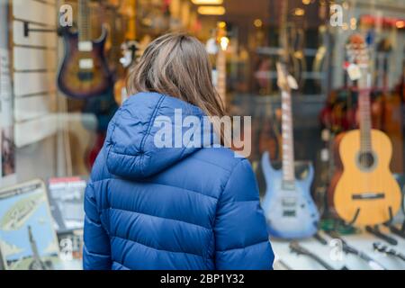 Musik-Verkauf-Konzept, Frau Wahl, die Entscheidung, eine neue Gitarre vor dem Instrumentengeschäft kaufen, Shop, Kauf einer neuen Gitarre Stockfoto