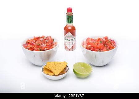 2 identische Schalen mit frisch zubereiteter Salsa mit einer Flasche Tabasco-Sauce, einer Schüssel Tortilla-Chips und einer halben Scheibe frischer Limette Stockfoto