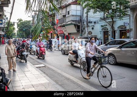 Hanoi, Vietnam - 30. April 2018: Straßenszene mit Einheimischen, die ihre Fahrräder oder Motorräder auf einer belebten Straße befreien. Stockfoto