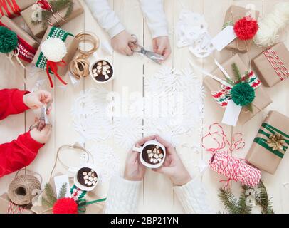 Mama mit Kindern Vorbereitung für Weihnachten. Wickelt Geschenkboxen und schneidet Schneeflocken aus Papier. Stockfoto