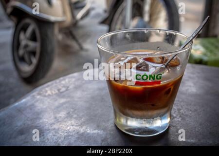 Vietnamesischer Kaffee im Glas mit Eis, mit verschwommenen Motorradrädern im Hintergrund, Hanoi, Vietnam Stockfoto