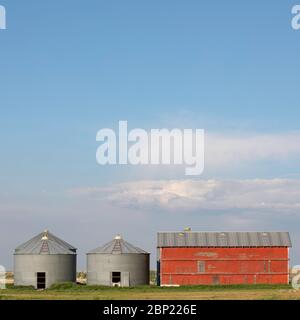 Zwei Getreidebehälter neben einer kleinen roten Scheune in den Prärien von Alberta Stockfoto