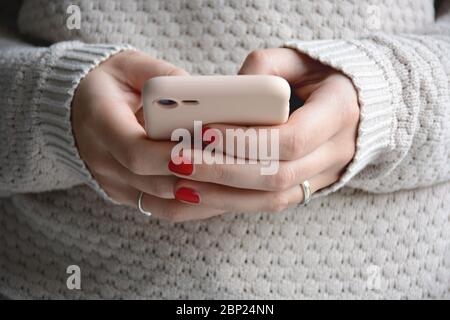 Nahaufnahme Frau mit roten Nägeln mit ihrem Handy. Senden einer Nachricht mit dem Smartphone. Vorderansicht Stockfoto