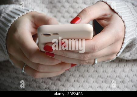 Nahaufnahme Frau mit roten Nägeln mit ihrem Handy. Senden einer Nachricht mit dem Smartphone. Vorderansicht Stockfoto