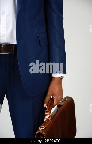 Nahaufnahme von stilvollen jungen dunkelhäutigen Geschäftsmann in blau formelle tragen Aktentasche halten. Business-Anzug. Vorderansicht, Mittelteil. Stockfoto