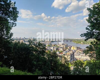 Kiewer Stadtbild mit Gebäudesilhouetten und Brücke über den Dnepr-Fluss unter blauem Himmel an einem Frühlingstag Stockfoto