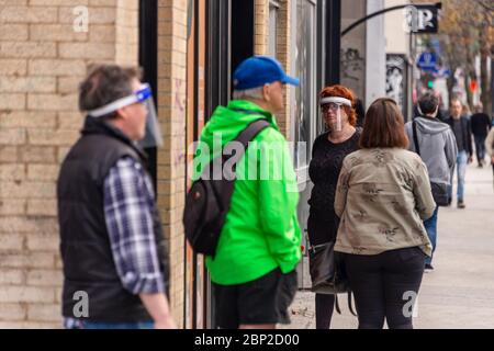 Montreal, CA - 16. Mai 2020 : Kunden in einer Linie außerhalb des Geschäfts. Einige von ihnen tragen Covid-19 Schutzschilde. Stockfoto