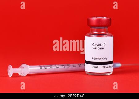 Coronavirus-Impfstoff-Konzept mit kleiner Flasche mit Text 'Covid-19-Impfstoff' mit Spritze in verschwommenem rotem Hintergrund Stockfoto