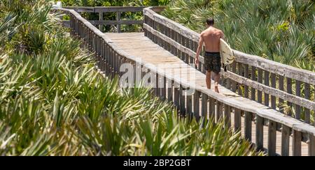 Surfer, die vom Strand über die Holzboardpromenade des Light House Point Park in Ponce Inlet, FL, zwischen Daytona Beach und New Smyrna Beach zurückkehren. (USA) Stockfoto