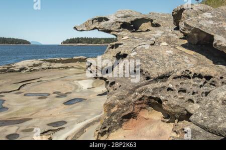 Eine seltsam geformte, raue Struktur Felsformation in BC's Flat Top Islands überblickt einen glatten Sandsteinstrand mit Gezeitenbecken, die bei Ebbe freigelegt sind. Stockfoto