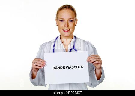 Eine junge Aerztin mit Stethoskop in ihrer Arztpraxis. Haelt ein leeres Schild mit der Aufschrift: Haende waschen Stockfoto