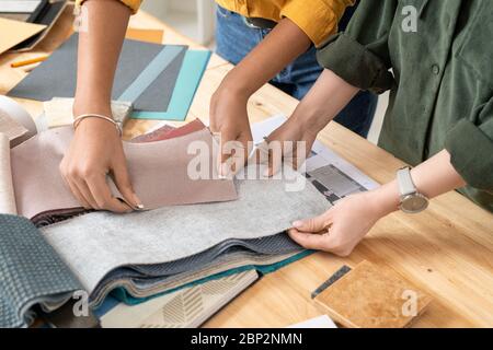 Zwei junge zeitgenössische Innenarchitektinnen, die Muster von Möbeltextilien durchsehen und sich für den Kunden eine aussuchen Stockfoto