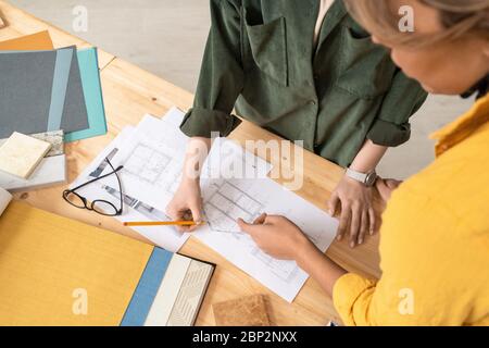 Zwei kreative Designerinnen, die sich über den Tisch beugen und bei Arbeitsbesprechung über Papiere mit Skizzen eines neuen Hauses oder einer Wohnung diskutieren Stockfoto