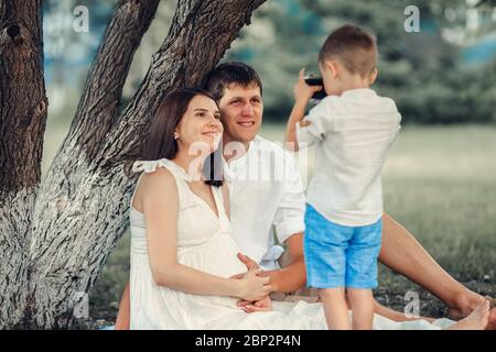 Ein junger Fotograf. Das Kind fotografiert an einem Sommertag unter einem Baum seine Mutter und seinen Vater. Stockfoto